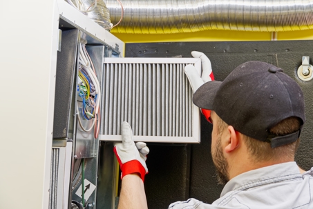 HVAC technician replacing an air conditioner furnace filter inside a residential HVAC system to improve indoor air quality and system efficiency.